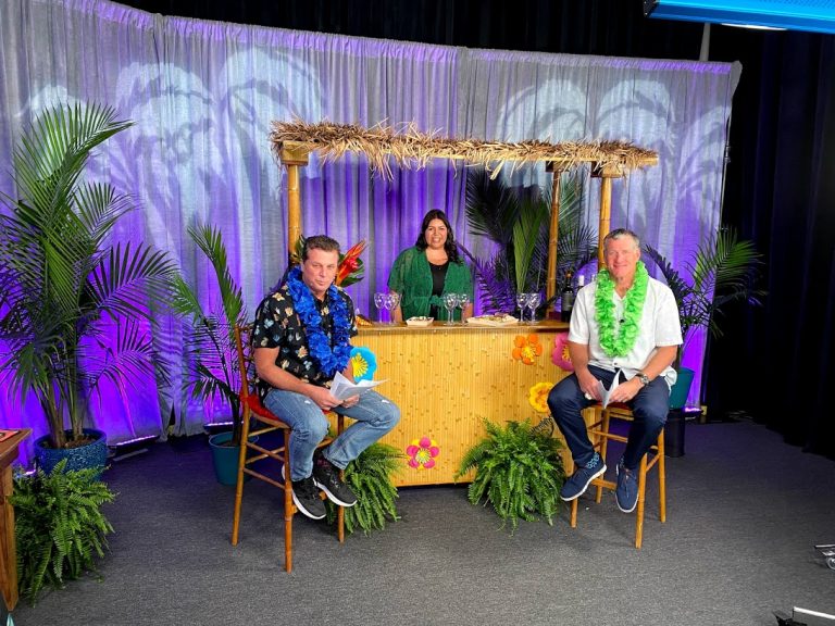 The hosts and sommelier sat at a tiki bar surrounded by palm trees in the center of the shot