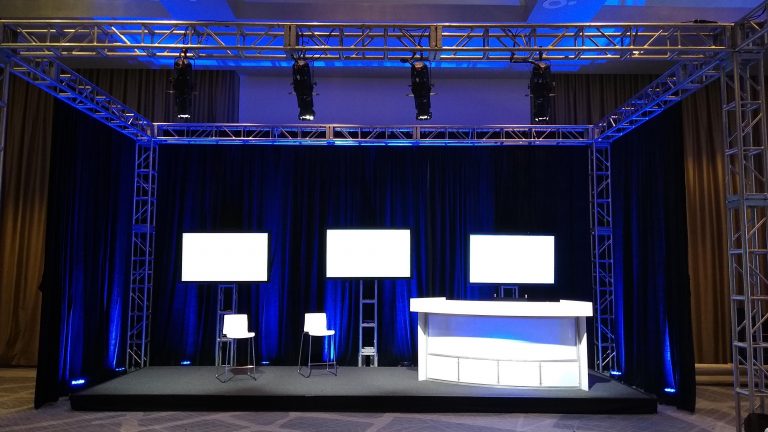 Set with a dark blue background, three screens, two white chairs, and one lounge.